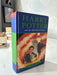A hardcover copy of the Harry Potter book, 'Harry Potter and the Half-Blood Prince', standing upright on a white marble-like surface. The book features a blue spine and front cover with green title text and a colorful illustration of characters surrounded by flames.