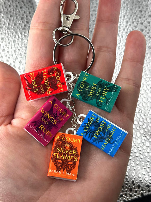 Keychain with book charm keyrings of 'A Court of Thorns and Roses' series held in a hand.
